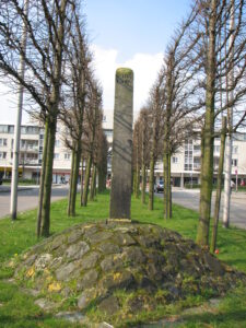 De (verplaatste) grenspaal van hoogheemraadschappen Schieland, Rijnland en Delfland, tussen de bomen, gezien richting winkelcentrum Rokkeveen aan de Reginagang.